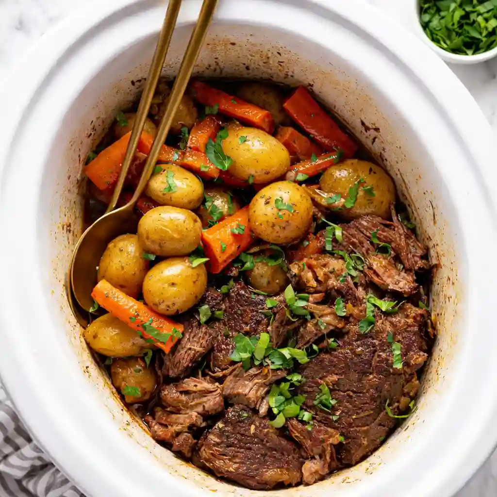 Easy Crock Pot Pot Roast slow cooked with carrots and onions on a white marble background