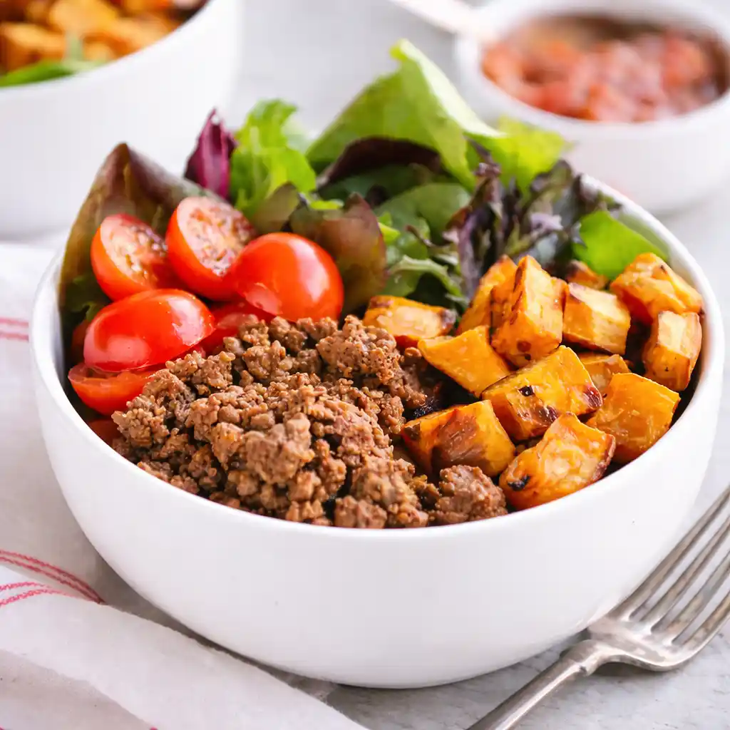 Ground beef and potato taco bowl with fresh toppings served on white marble background