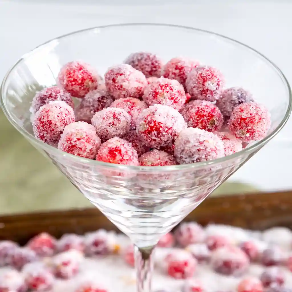 Orange vanilla candied cranberries sparkling in a glass bowl on white marble background