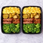 Meal prep containers with Human Kibble Breakfast Box including scrambled eggs, roasted potatoes, and broccoli