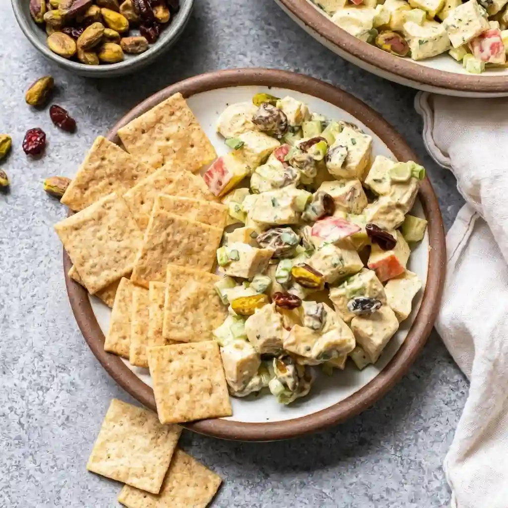 A clean overhead view of a white ceramic bowl filled with creamy classic chicken salad on a bright white marble background.