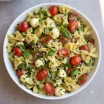 A clear glass mason jar filled with vibrant creamy bow tie pasta salad ready for a quick lunch on a white countertop.