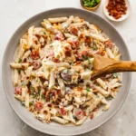 A clear glass mason jar filled with vibrant creamy million dollar pasta salad ready for a quick lunch on a white countertop.