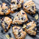 An opened glass meal prep container displaying two fresh, quick baked scones glazed lemon blueberry.